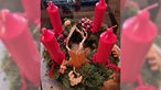 Ein Adventskranz aus Tannenzweigen mit langen roten Kerzen.
