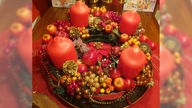 Ein Adventskranz mit roten Kugeln, Kerzen und künstlichen Früchten dekoriert.