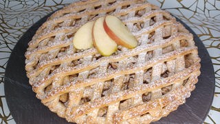 Ein Apple Pie mit einem feinen Teiggitter mit Puderzucker auf einem weiß-golden gemusterten Untergrund