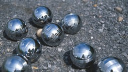 Acht silberfarbende Boule-Kugeln auf dem Boden liegend.