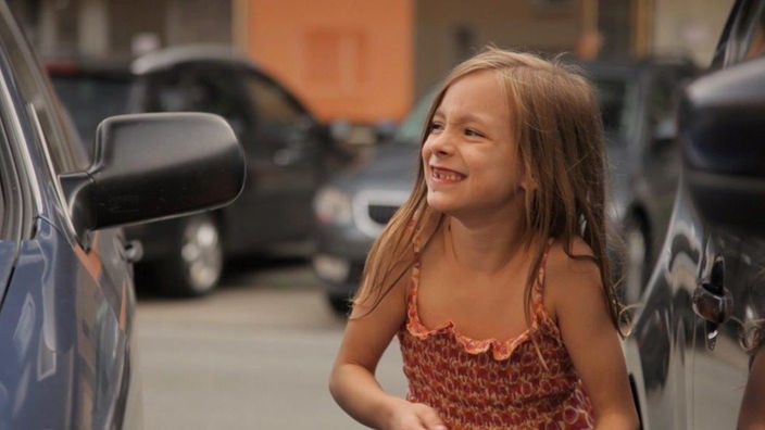 Ein kleines blondes Mädchen steht neben einem Auto
