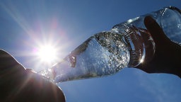 Frau trinkt aus einer Wasserflasche. Gegenlichtaufnahme. Sonne im Hintergrund.