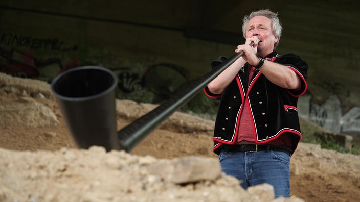Musiker Roland Pütz bläst Alphorn unter einer Brücke