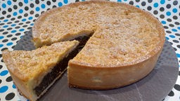 Ein angeschnittener Mohnkuchen mit Streuseln auf einer Kuchenplatte