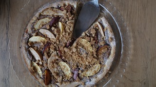 Ein Obst-Kekscreme-Kuchen auf einem Glasteller, angeschnitten, mit Kuchenschaufel