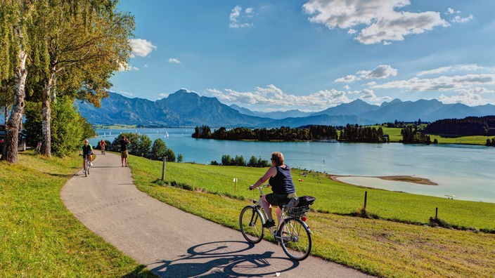 Radfahrerin vor einer Berg-und Seenlandschaft in Bayern.