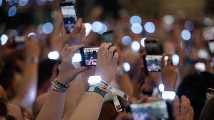 Zuschauer filmen während des Konzerts von Sängerin Taylor Swift in Gelsenkirchen 2024 mit ihren Smartphones.