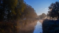 Auf einem See spiegeln sich die umstehenden Bäume in herbstlichen Farben und der blaue Himmel