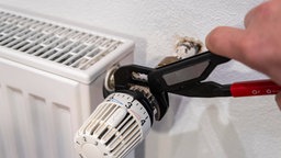 Hand mit Zange an Heizkörperthermostat