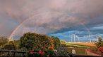 Blick von einem Balkon auf einen Regenbogen über einem Feld.