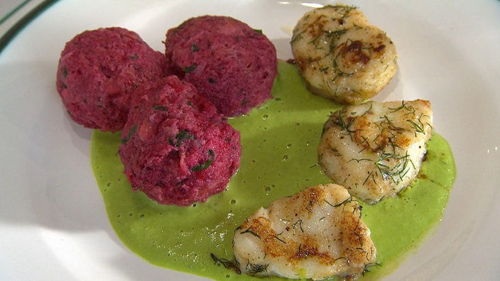 Drei Rote Bete-Knödel mit gebratenen Fischstücken und grüner Soße auf einem Teller angerichtet