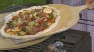 Pizza wird mit einem Holzbrett auf den Pizzastein befördert
