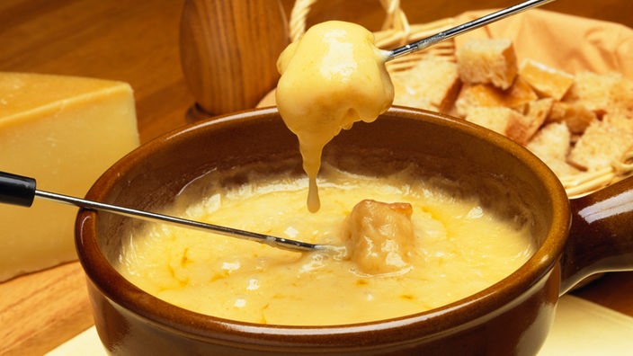 Käsefondue - ein Brotwürfel wird mit einer Gabel in einen Fonduetopf mit Käse getaucht