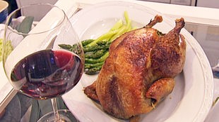 Gebratenes Perlhuhn mit grünem Spargel auf einem Teller angerichtet, daneben ein Glas Rotwein