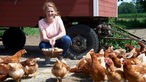 Andrea Strothlüke mit einem Korb Eier inmitten von freilaufenden Hühnern. 