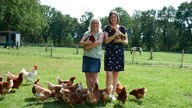 Silvia und Anna mit Huhn auf dem Arm inmitten von Hühnern