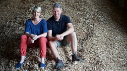 Anne Lee-Bolhöfer sitzt mit ihrem Mann auf einem Berg Holzschnitzel.