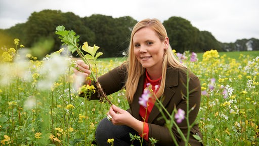 Annika Ahlers auf einem Feld mit einer Pflanze in der Hand. 