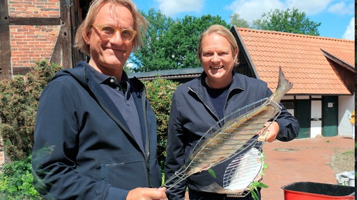 Frank Buchholz (l) und Björn Freitag bereiten für das Jubiläums-Dinner regionale Lachsforellen auf dem Grill zu.