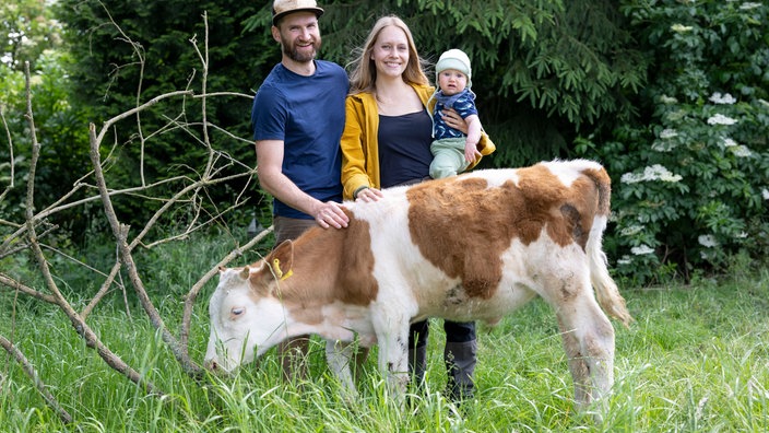 Melvin Berger mit seiner Frau Friedericke und Sohn Nuka und einer Kuh auf der Weide. 