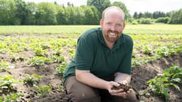 Rainer Overkämping mit einer Handvoll Erde auf dem Feld. 