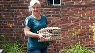 Silvia Mölders trägt mehrere volle Eierkartons.