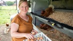 Stephie Bönniger sammelt Eier aus einem mobilen Hühnerstall.