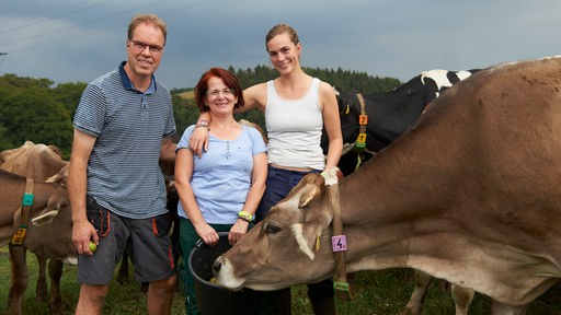 Zwei Frauen und ein Mann mit Kühen im Hintergrund