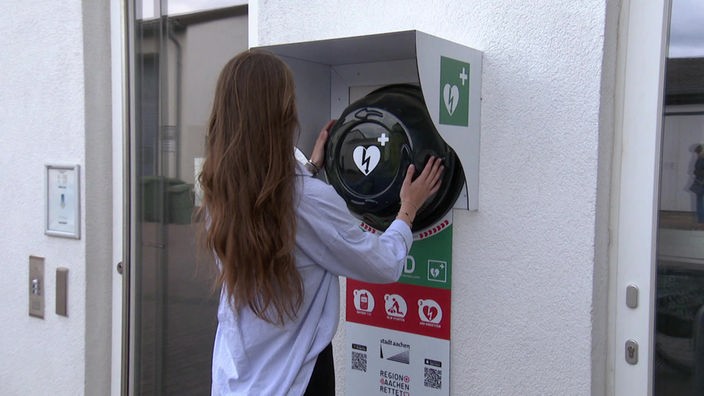 Eine Frau nimmt den Defibrillator von der Wand