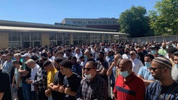 Eine große Menge an Männern stehen trauernd vor einem Gebäude.