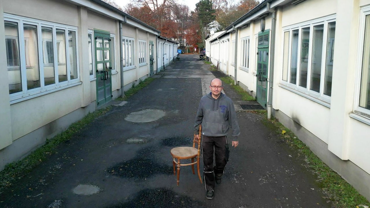 Udo Schmitz trägt einen Holzstuhl in die Schreinerei