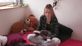 Annalena sitzt auf ihrem Bett und liest ein Buch