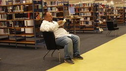 Oliver Meise sitzt in der Bibliothek und liest ein Buch