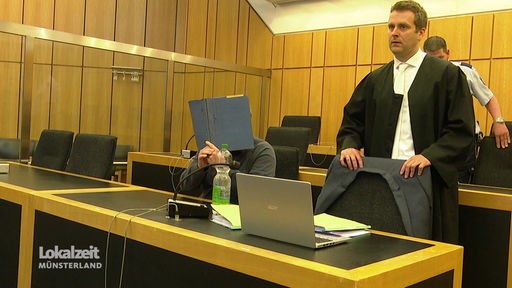 Der Angeklagte im Gerichtssaal verdeckt sein Gesicht mit einem Mappe