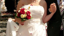 Braut mit Brautstrauß und Bräutigam im Konfettihagel beim Gang aus der Kirche