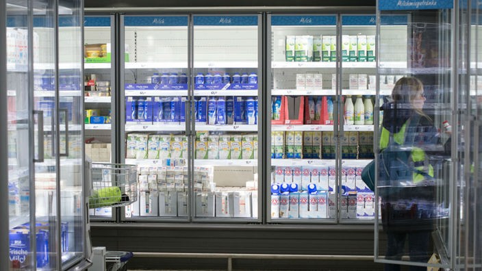 Eine Frau steht vor einem großen Milchregal im Supermarkt.