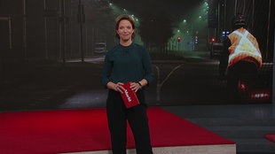 Anna Planken  steht im Markt-Studio. Im Hintergrund sieht man ein Bild von einer Person, die Nachts Fahrrad fährt.