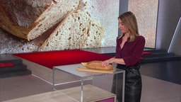 Catherine Vogel steht im Markt-Studio und schneidet ein Laib Brot.