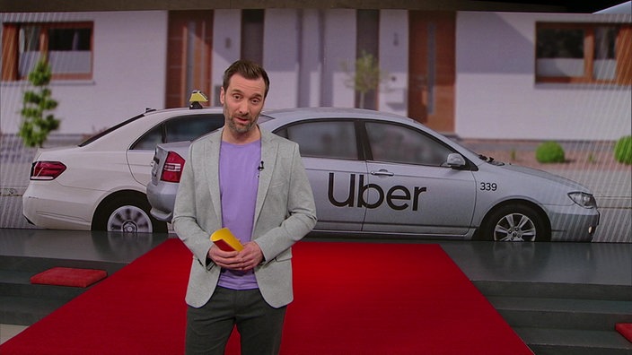 Daniel Aßmann steht im Markt-Studio. Im Hintergrund sind zwei Autos abgelichtet.