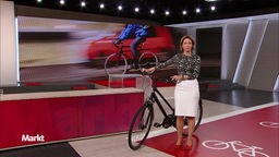 Die Moderatorin shte im Studio mit einem Schwarzen Fahrrad. 