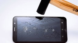 Das Bild zeigt ein gebrochenes Smartphonedisplay und einen Hammer darüber.