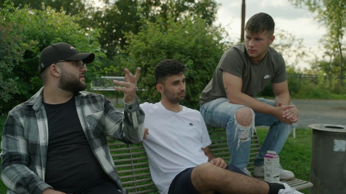Drei junge Männer sitzen auf Park Bank und unterhalten sich.