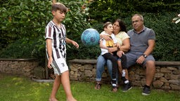 Rafael spielt Fußball während der Rest der Familie auf der Mauer im Garten sitzt.