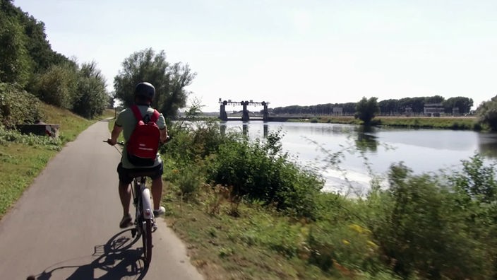 Daniel Aßmann radelt auf einem Fahrradweg entlang eines Gewässers