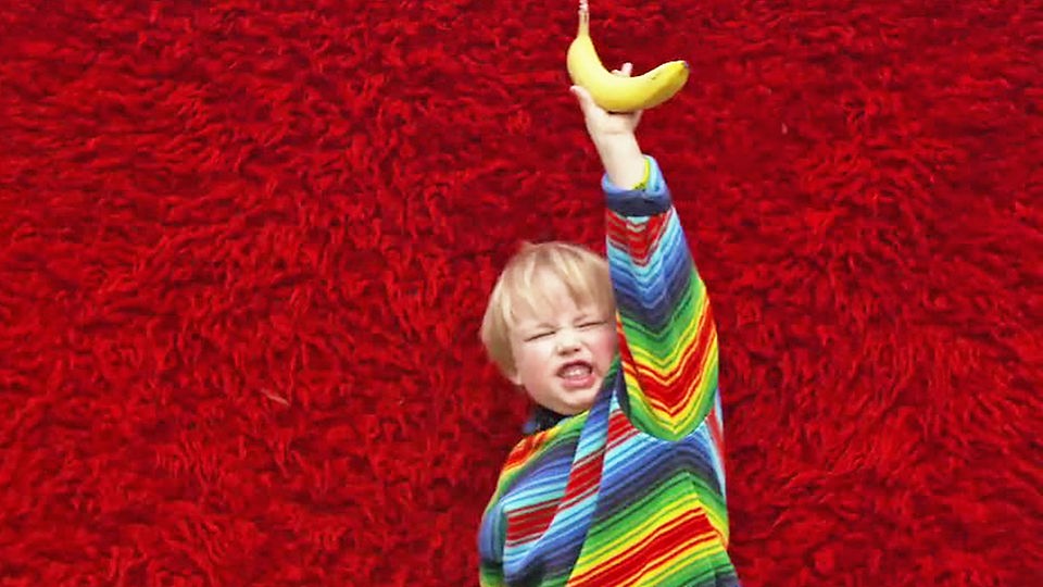 Junge vor rotem Hintergrund hält Banane in die Luft