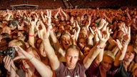 Eine Menschenmenge, die mit erhobenen Händen jubelnd zur Kamera guckt