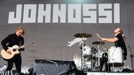 Drummer und Gitarrist von Johnossi spielen nebeneinander auf der Bühne. Im Hintergrund das "Johnossi" - Logo