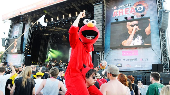 Ein Zuschauer in einem Elmo-Kostüm sitzt auf den Schultern eines weiteren Zuschauers, der als Teufel verkleidet ist