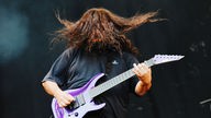 Gitarrist der Band Deftones wirft seinen langen Haare nach vorne, sodass man sein Gesicht nicht erkennen kann