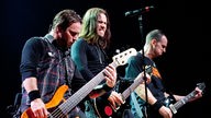 Drei Bandmitglieder von Alter Bridge spielen Bass und Gitarre auf der Bühne
